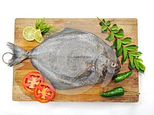 Fresh Black Pomfret Fish decorated with herbs and vegetables on a wooden pad Selective focus photo
