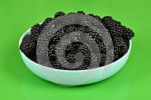 Fresh blackberry in plactic bowl on geen background