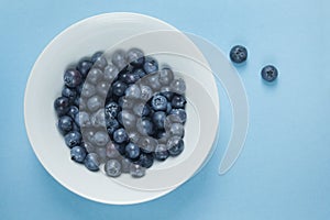 Fresh blueberries in a bowl on blue background.