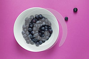 Fresh blueberries in a bowl on pink background.