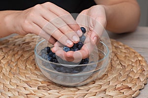 Fresh Blueberries in a Glass Bowl in Female Hands. Picking ripe blueberries from a glass bowl