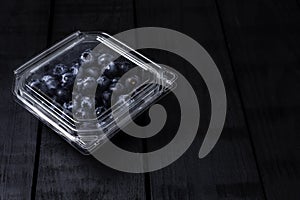 Fresh blueberries inside plastic container on black background