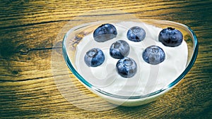 Fresh blueberries in low fat yogurt on a wooden background