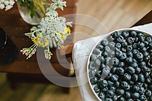 Fresh blueberries on modern ceramic plate and wildflowers bouquet in rustic room. Food aesthetics