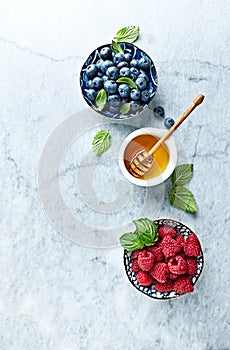 Fresh Blueberries and Raspberries with Honey and Mint Leaves on gray marble background. Flat lay. Healthy Diet Concept.