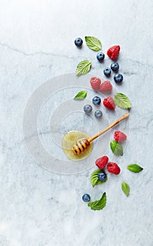 Fresh Blueberries and Raspberries with Honey and Mint Leaves on gray marble background. Flat lay. Healthy Diet Concept.