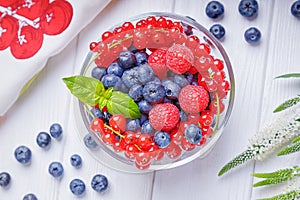 Blueberries, raspberries and red currant in a bowl on a white wooden background. Top view