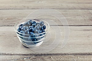Fresh blueberries in small transparent glass bowl placed on wood