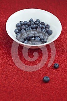 Fresh blueberries in a white bowl on red glittering background.