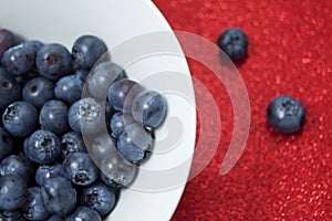 Fresh blueberries in a white bowl on red glittering background.