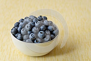 Fresh blueberries in a white ceramic bowl on a yellow crackle background