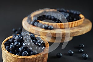 Fresh blueberries in a wooden bowl next to blueberry tart on a wooden stand