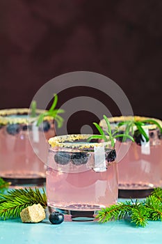 Fresh blueberry cocktail with rosemary and ice in glasses with decorate brown sugar on turquoise surface and black background.