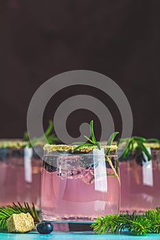 Fresh blueberry cocktail with rosemary and ice in glasses with decorate brown sugar on turquoise surface and black background.