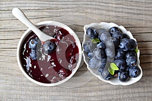 Fresh blueberry jam in a white bowl and freshly picked blueberries on a wooden table. Homemade food concept.