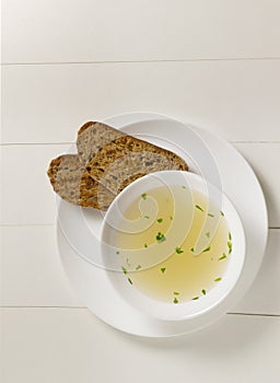 Fresh bouillon in a white plate with finely chopped greens and croutons on a white background. Copy space. photo