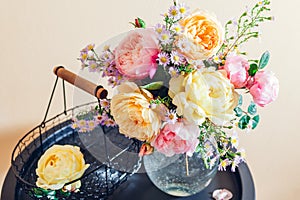 Fresh bouquet of roses flowers put in glass vase on table. Close up of pink yellow blooms with basket. Interior decor