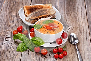 Fresh bowl of creamy tomato soup and sandwich with basil leaves