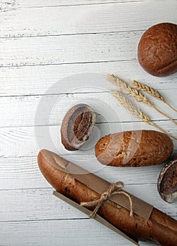 Fresh bread - buns, baguette and ears of wheat on wooden background flat lay. Vertival image