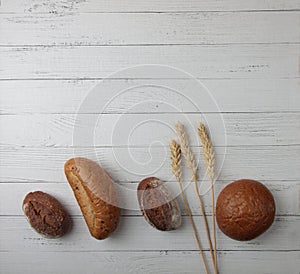 Fresh bread - buns, baguette and ears of wheat on wooden background flat lay. Vertival image