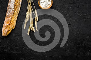 Fresh bread concept. Crispy french baguette near ears of wheat and bowl with flour on black background top view copy