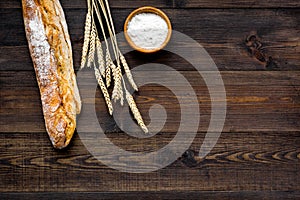 Fresh bread concept. Crispy french baguette near ears of wheat and bowl with flour on dark wooden background top view