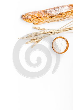 Fresh bread concept. Crispy french baguette near ears of wheat and bowl with flour on white background top view copy