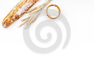 Fresh bread concept. Crispy french baguette near ears of wheat and bowl with flour on white background top view copy