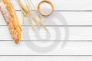 Fresh bread concept. Crispy french baguette near ears of wheat and bowl with flour on white wooden background top view