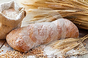 Fresh bread, flour and wheat ears on wooden table.