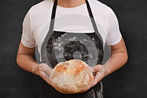 Fresh bread in the hands of a baker on a black background. Preparing cooking