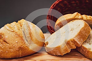 Fresh bread made from wheat flour in a wicker basket made of dark wood lies on a wooden board and against a dark background. Light