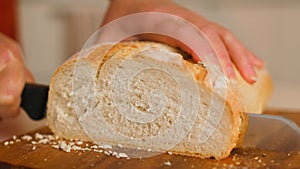 Fresh bread slice and cutting knife on table. Female hands cutting wheaten bread on the wooden board, selective focus