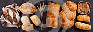 Fresh bread with wheat ears on dark table, top view