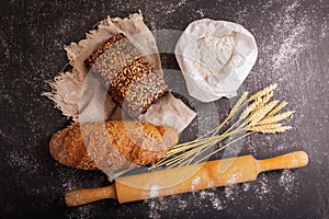 Fresh bread with wheat ears, flour and kitchen utensils on dark board