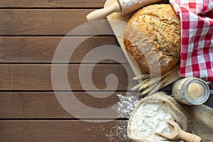 fresh bread with wheat ears and sack of flour, yeast, rolling pin on dark table, top view
