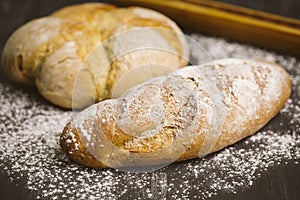 Fresh breads on dark wood with sprinkled flour.