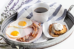 Fresh breakfast with bacons, eggs, a cup of coffee, and pancakes with cream on the tray