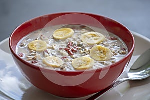 Fresh breakfast of granola, yogurt, nuts, goji berries, chia seeds and banana. Muesli with fruits and berries in red bowl