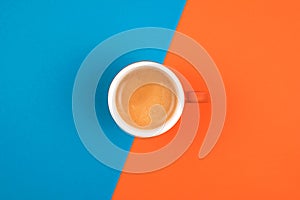 Fresh brewed coffee in ceramic cup over orange and blue background. Place for text