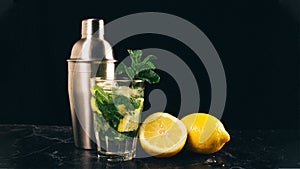 Fresh bright summer cocktail. Mojito cocktail with lemon, metal cocktail shaker and lemons on a fashionable stone black