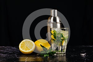 Fresh bright summer cocktail. Mojito cocktail with lemon, mint in a glass, metal cocktail shaker on a fashionable stone