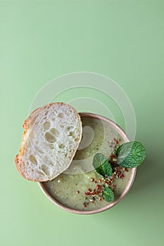 Fresh broccoli cream soup served with fresh bread, mint and spices in craft container on green background. Soup to go, healthy