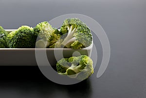 Fresh broccoli is housed in white ceramic vessels and placed on a black floor. Space for text.