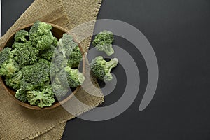 Fresh Broccoli in wooden bowl and seed oil in rustic style. Close up on a black background. copy space for text. Top