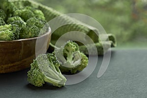 Fresh Broccoli in wooden bowl and seed oil in rustic style. Close up on a black background. side view, harvest