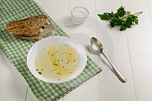 Fresh broth in a white plate with finely chopped greens on a green checkered towel on a white background. photo