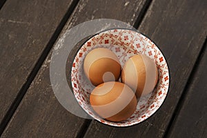 Fresh brown eggs in a beautiful bone china bowl on brown acacia wood planks