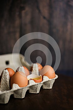 Fresh brown eggs and a broken egg with yolk in an eco tray made from recycled paper on a dark wooden background