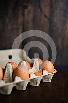 Fresh brown eggs and a broken egg with yolk in an eco tray made from recycled paper on a dark wooden background